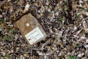 A hard drive lies on a pile of shredded electronic waste.